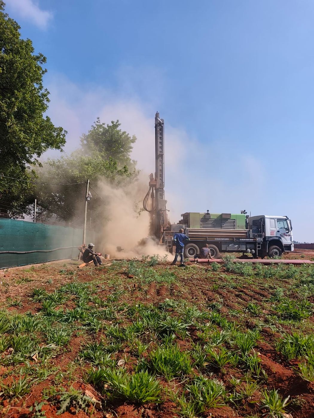 Drilling rig with dust cloud beside a green field